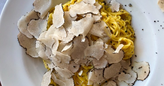 Shaved black truffle on a plate of fresh pasta, accompanied with a glass of wine on a wine and truffles foodie tour